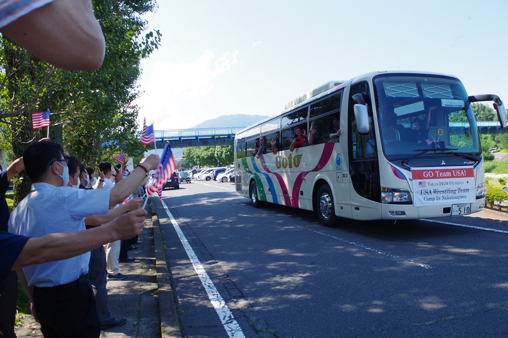 市役所前で職員が旗を振ってバスが通過しています