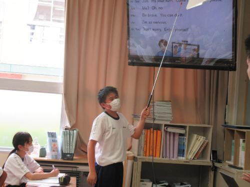 棒でテレビ画面を指し説明する生徒