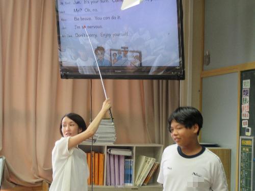 棒でテレビ画面を指し説明する生徒