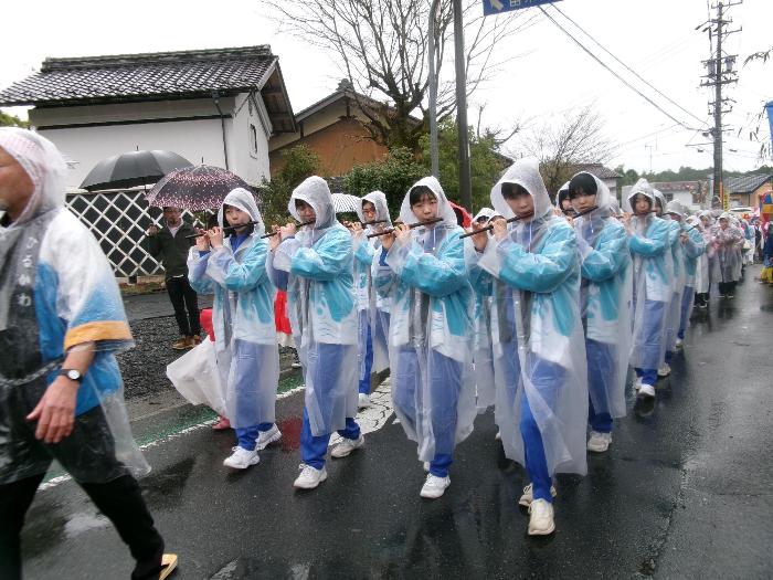 雨の中、沿道を練り歩きながら演奏する中学生