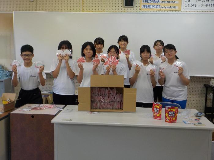 作ったプレゼントを両手に持ち集合写真を撮る中学生