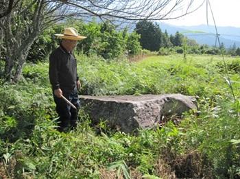 草むらの中に置かれた石と、地元の人の画像
