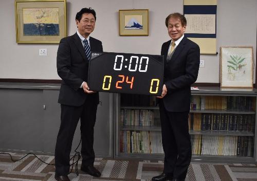 デンソーテン株式会社の職員と教育長がバスケットボールで使用するタイマーを持っている様子