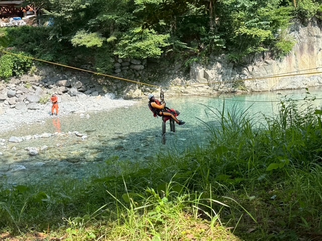 要救助者に模した人形と、隊員がロープにぶらさがり、中洲から岸側へ救出される様子。